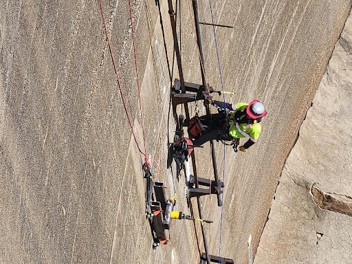 BDI engineer watching anchor tension testing equipment during tension testing of anchor at downstream dam surface using rope access